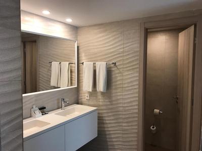 Bagno moderno con lavabo bianco, grande specchio e asciugamani appesi al muro.
