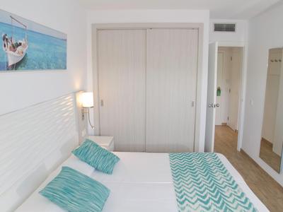 Nowoczesny pokój hotelowy z podwójnym łóżkiem, turkusowymi wzorzystymi poduszkami i kocem, jasną drewnianą podłogą.