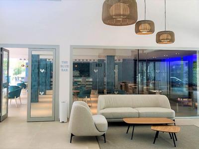 Area lounge dell'hotel luminosa con divano bianco, poltrona e tavoli moderni in legno davanti a parete in vetro.