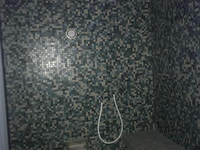 Stanza doccia con piastrelle a mosaico grigie e una panca contro la parete destra.