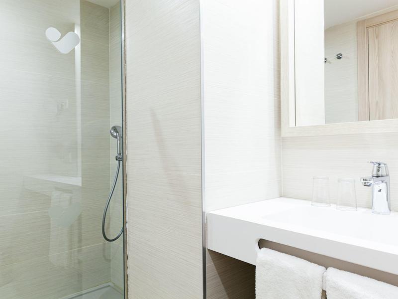 Bagno moderno con doccia, lavabo e asciugamani in bianco e grigio chiaro.