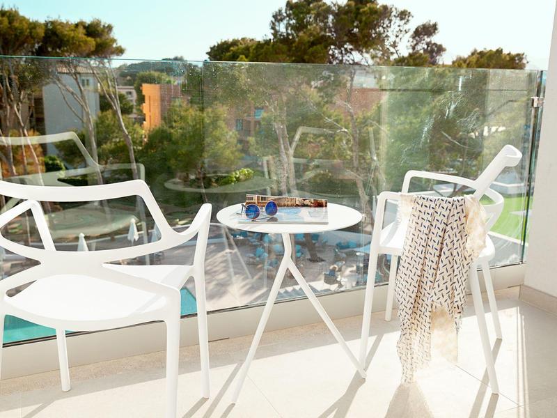 Balcone moderno con due sedie bianche, un piccolo tavolo e vista sugli alberi.