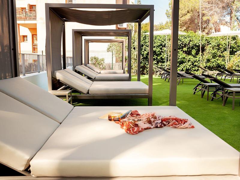 Lettini luminosi sotto gazebo coperti vicino a una piscina d'hotel con prato verde.