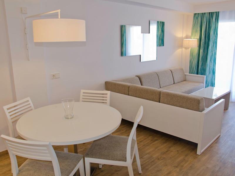 Soggiorno luminoso con tavolo da pranzo rotondo e divano grigio contro pareti bianche e pavimento in legno.