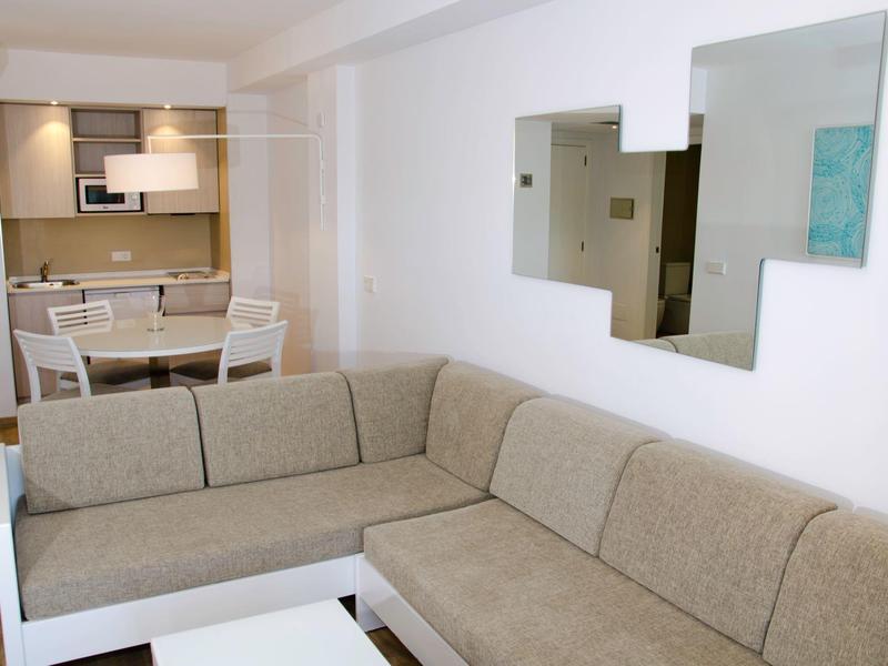 Soggiorno moderno con divano ad angolo beige, tavolo bianco e zona pranzo sullo sfondo.