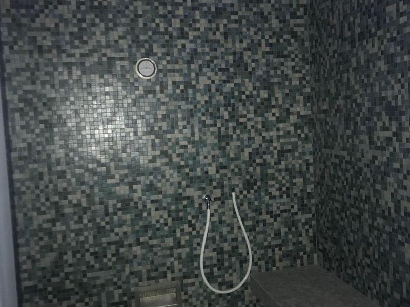 Stanza doccia con piastrelle a mosaico grigie e una panca contro la parete destra.