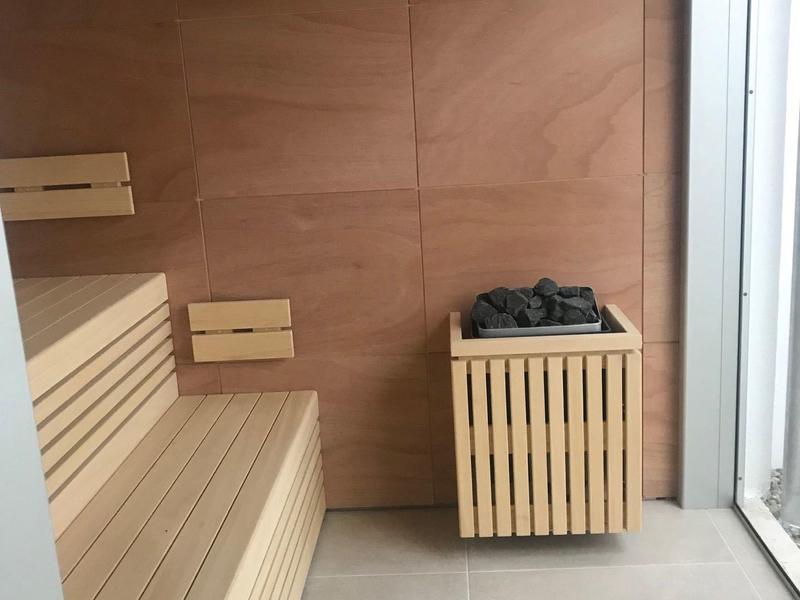 Stanza sauna moderna con panche in legno e stufa da sauna accanto a parete in vetro