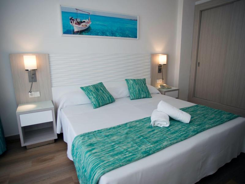 Camera d'hotel moderna con letto matrimoniale, accenti turchesi e illuminazione soffusa.