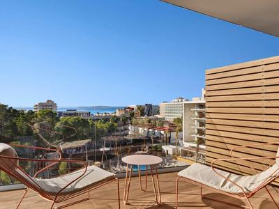 Balcone con due sdraio e piccolo tavolo, vista sulla città e sul mare sullo sfondo.
