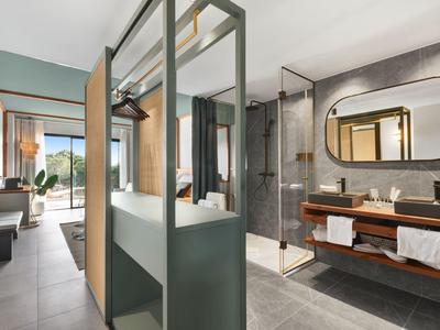 Bagno moderno in hotel con doccia in vetro e vista su un soggiorno con balcone.