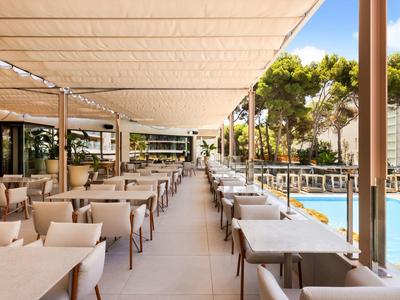 Ampia terrazza coperta con tavoli apparecchiati accanto a una piscina e alberi sullo sfondo.