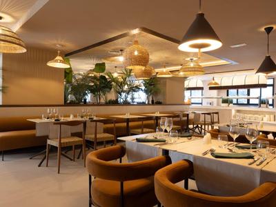 Area ristorante di hotel moderno con tavoli rotondi, sedie e illuminazione calda