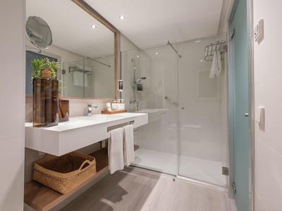 Bagno luminoso con lavabo doppio, parete a specchio e doccia con vetro.