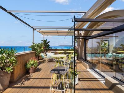 Terrazza con vista mare, pavimento in legno e mobili da giardino moderni sotto il cielo blu.