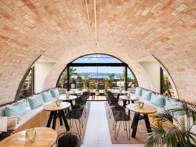Ristorante luminoso con soffitto ad arco, tavoli in legno e vista su terrazza e mare.