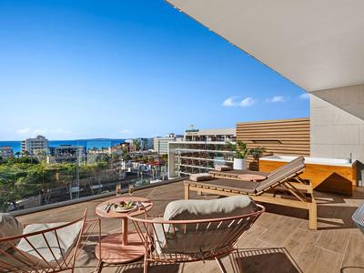 Balcone con sedie e lettino con vista sul mare e edifici moderni sotto un cielo sereno.