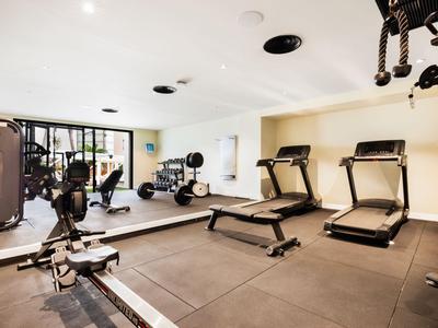 Lichte fitnessruimte met loopbanden, gewichtbank en spinningfiets voor glazen wand.