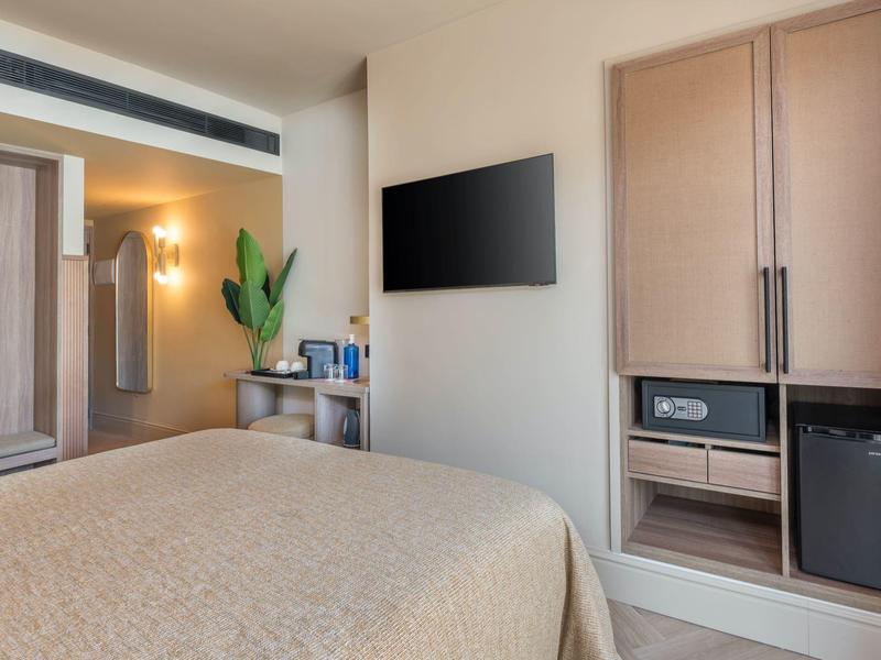 Camera d'hotel moderna con letto, TV a parete, armadio e minibar.