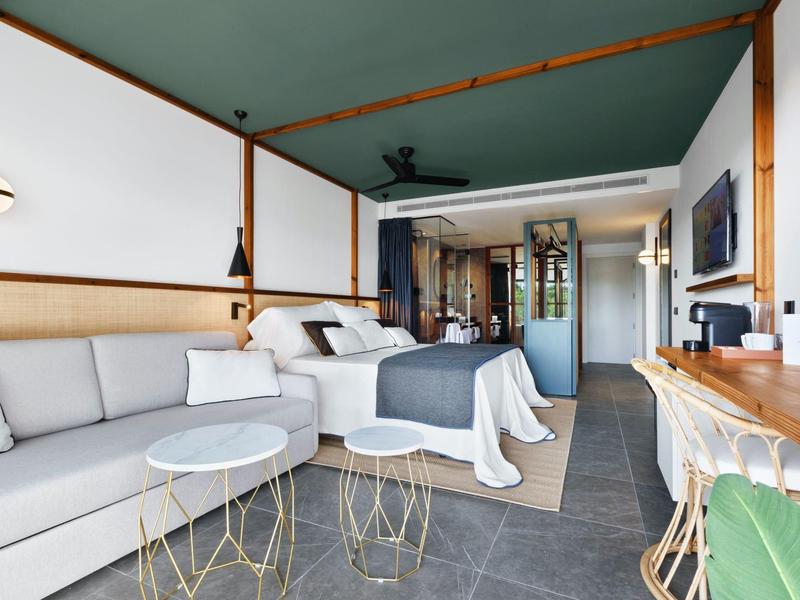 Camera d'hotel moderna con letto, divano e scrivania in colori tenui