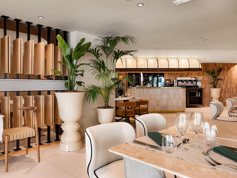 Ristorante d'hotel moderno con tavoli eleganti, sedie e piante in tonalità neutre.