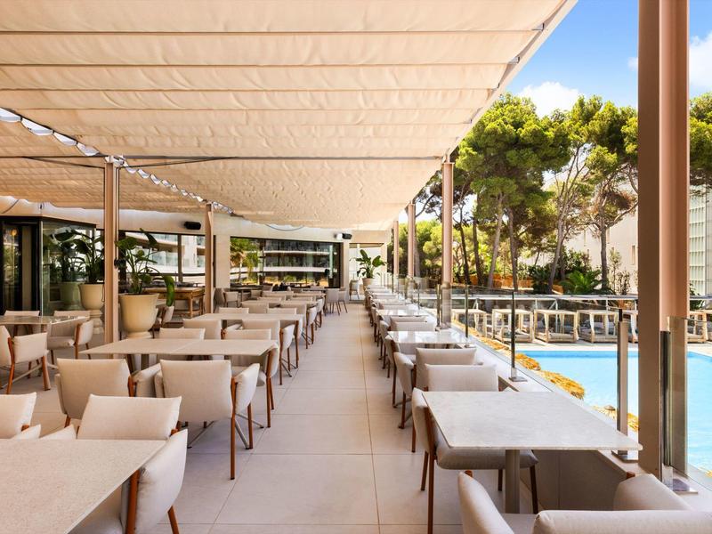 Ampia terrazza coperta con tavoli apparecchiati accanto a una piscina e alberi sullo sfondo.