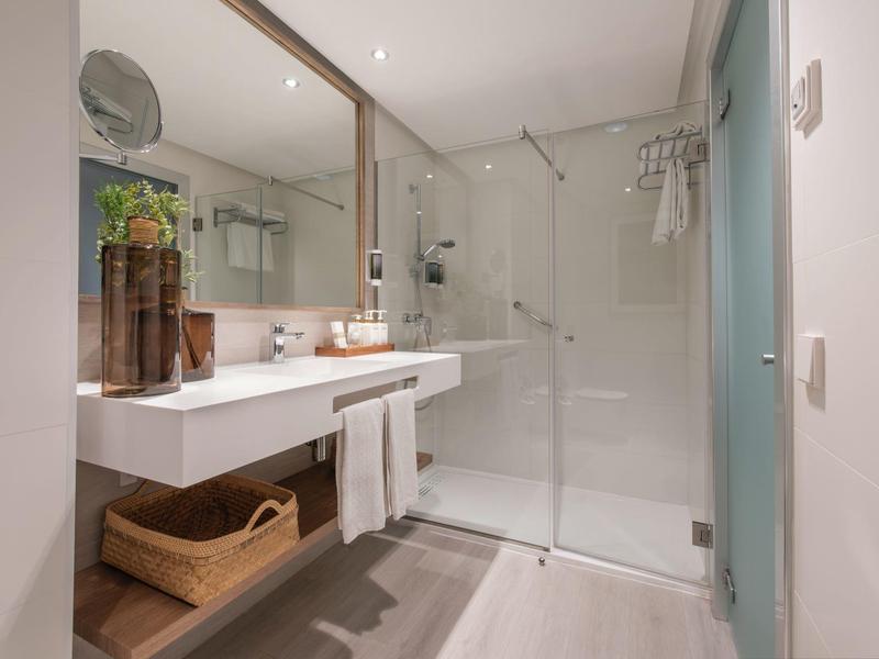 Bagno luminoso con lavabo doppio, parete a specchio e doccia con vetro.