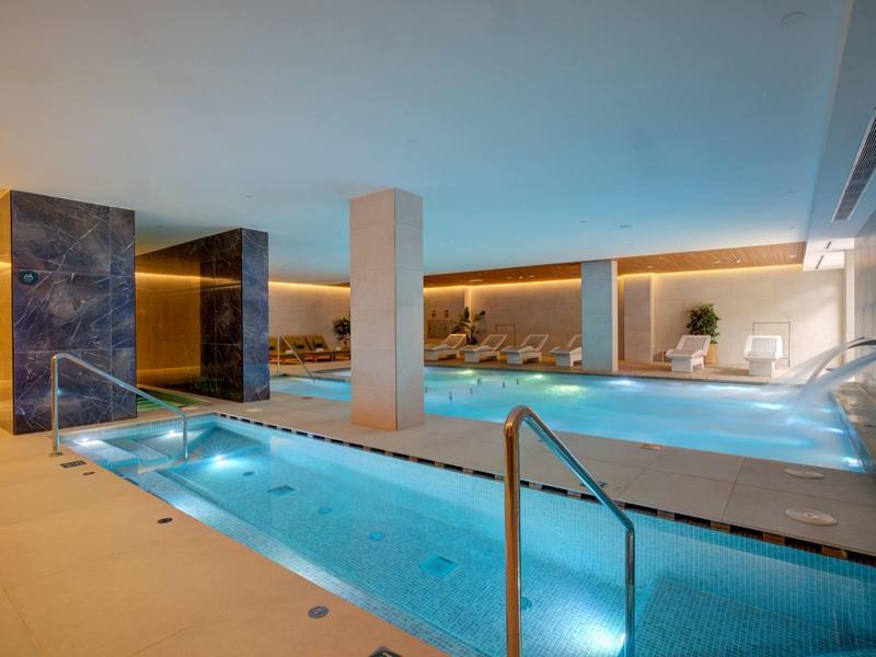 Area piscina interna moderna con piscina riscaldata, vasca idromassaggio e aree relax.