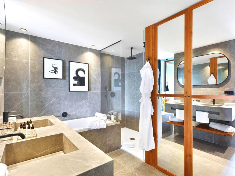 Bagno moderno con doppi lavandini, ampia doccia e dettagli in legno chiaro.