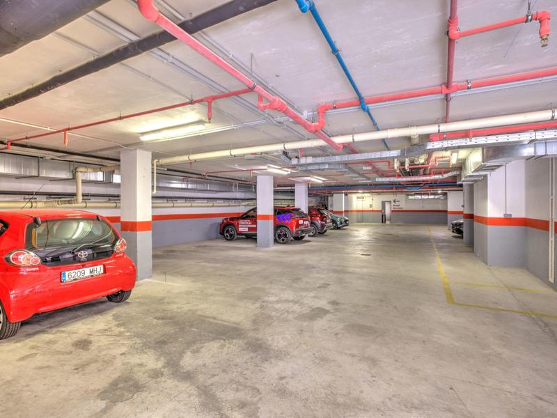 Autorimessa sotterranea luminosa con diverse auto parcheggiate e tubi rossi e blu sul soffitto.