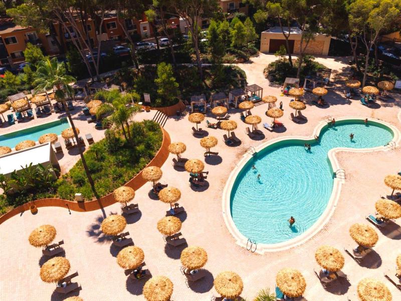 Una piscina di hotel con ombrelloni rotondi di paglia e lettini in un ambiente tropicale.