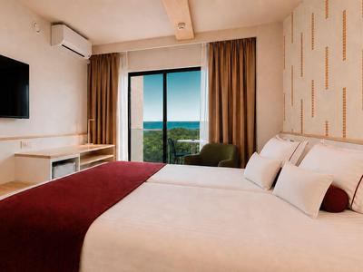 Modernes Hotelzimmer mit großen Betten, Fernseher und Blick auf die Natur durch den Balkon.