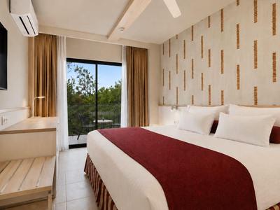 Modern eingerichtetes Hotelzimmer mit großem Bett, Flachbildfernseher und Balkon mit Blick ins Grüne.