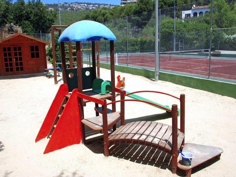 Area giochi colorata per bambini accanto a un campo da tennis all'aperto con sabbia.