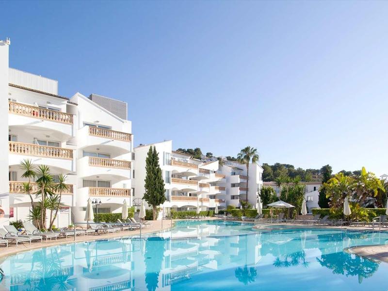 Complesso alberghiero moderno con ampia piscina, ombrelloni e palme sotto un cielo sereno.