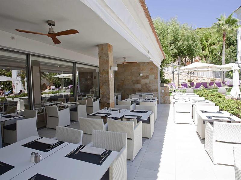 Area esterna moderna di un hotel con tavoli e sedie bianche in una giornata soleggiata.