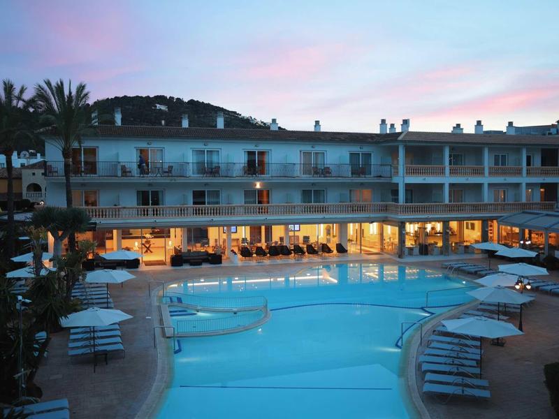 Hotel con piscina illuminata e lettini al crepuscolo.