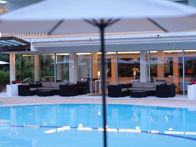 Area esterna moderna con piscina e ombrellone davanti a una terrazza d'hotel con posti a sedere.