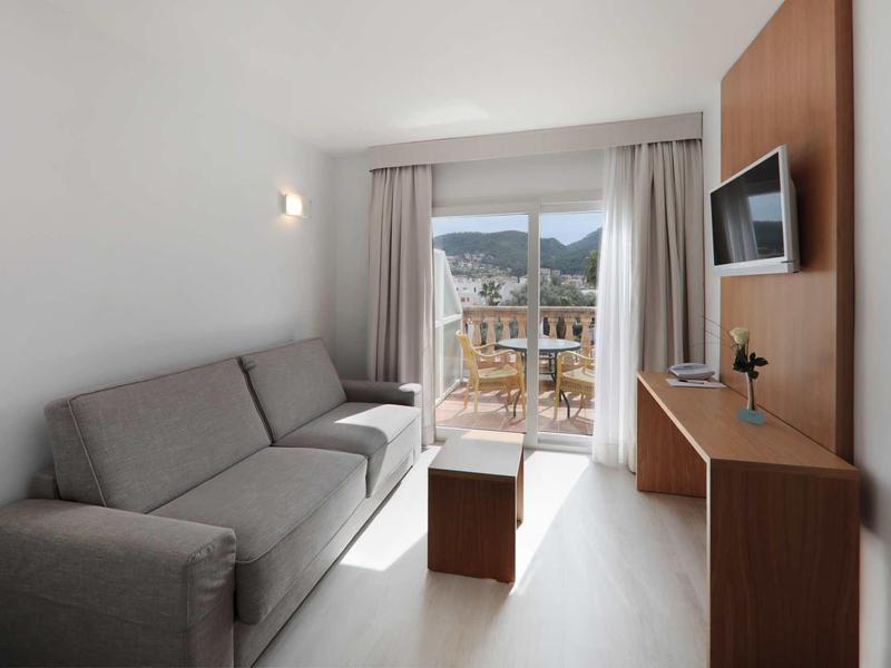 Soggiorno luminoso con divano grigio, mobili in legno e balcone con vista sulle montagne.