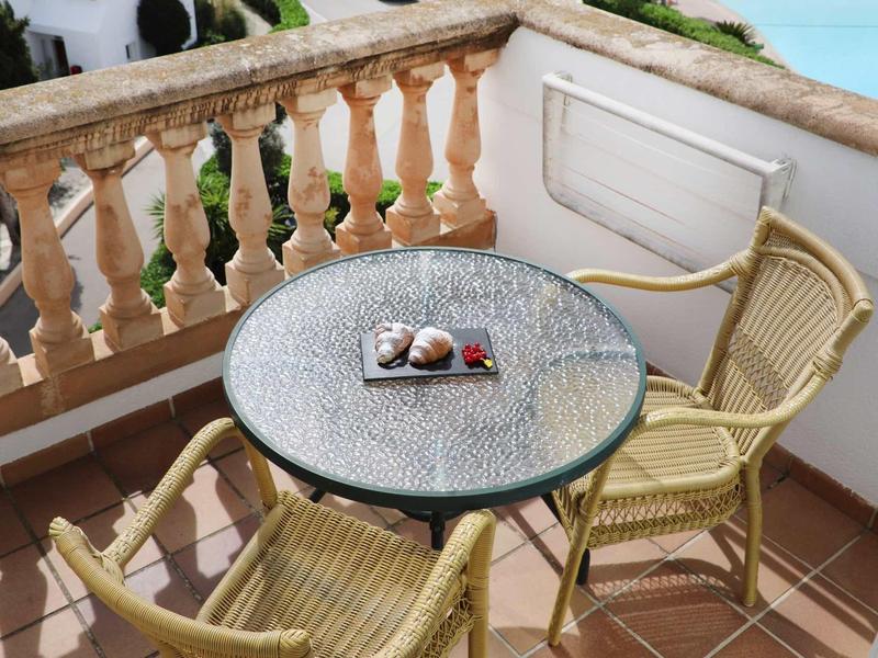 Balcone con tavolo rotondo in vetro e due sedie intrecciate, vista mare sullo sfondo.