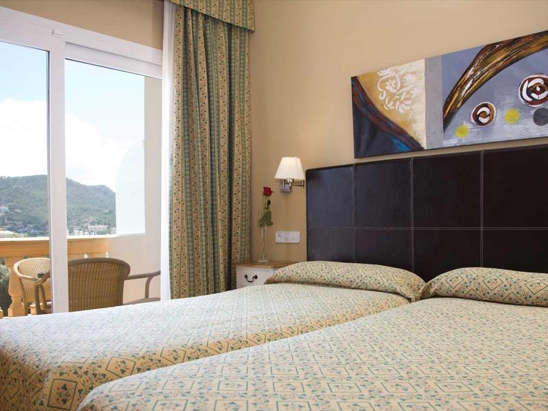 Camera d'hotel con due letti, balcone con vista mare e decorazioni murali moderne.