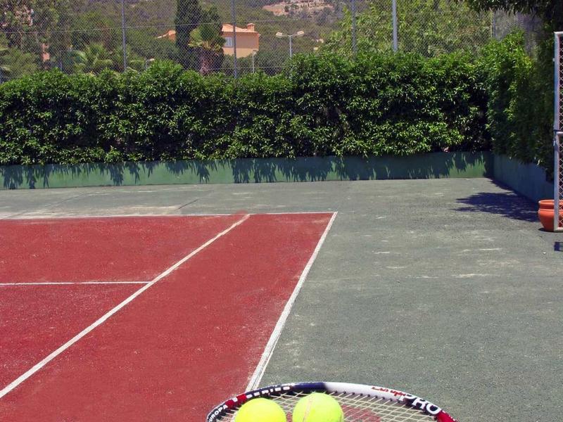 Campo da tennis all'aperto con racchetta e palline in primo piano, montagne sullo sfondo