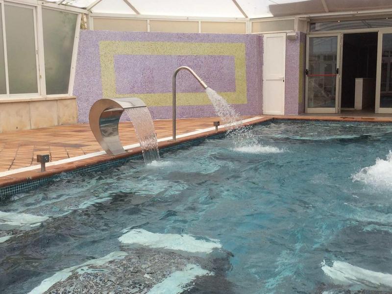 Innenpool mit Wasserdüsen, Edelstahl-Massagebank und großer Glasüberdachung.