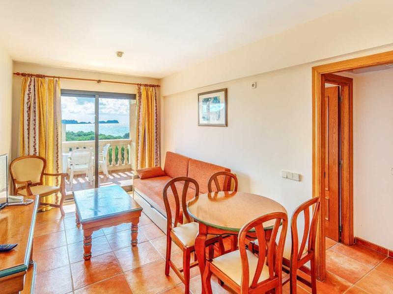 Helles Wohnzimmer mit Holzmöbeln, orangem Sofa, Glas-Tisch und Balkon mit Ausblick.