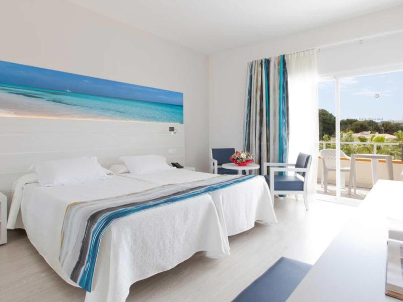 Heller Hotelraum mit Doppelbett, blauer Meeresbild-Dekoration und Terrasse mit Aussicht.