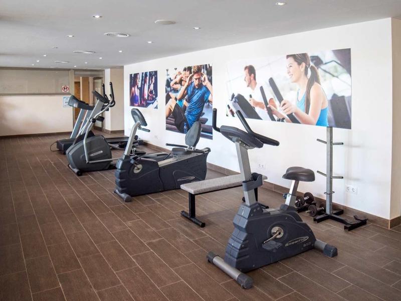 Moderner Fitnessraum mit Laufband, Fahrrädern und Wandbild mit Sportmotiven.