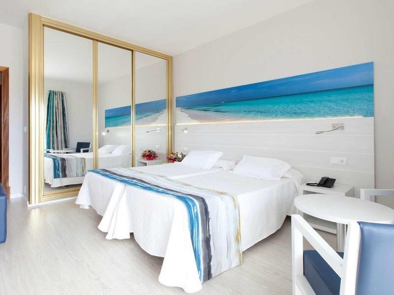 Modernes Hotelzimmer mit Doppelbett, großem Spiegel, blauer Dekoration und Meer-Wandbild.