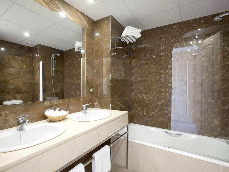 Moderne Bad mit braunen Fliesen, Doppelwaschbecken, Badewanne und großer Spiegel.