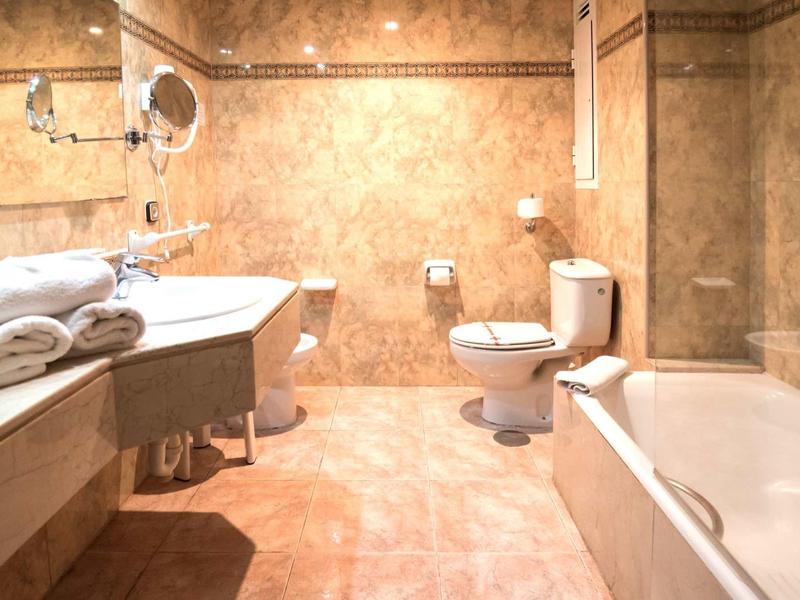 Helles Badezimmer mit beiger Marmoroptik, zwei Waschbecken, Toilette und Badewanne.