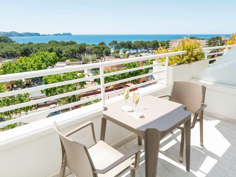 Balkon mit zwei Stühlen, Tisch und Blick auf grünes Gelände und das blaue Meer im Hintergrund.