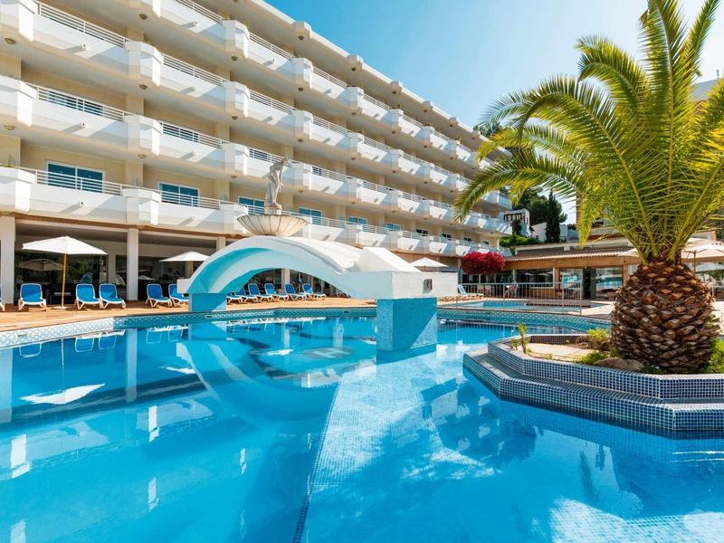 Moderner Hotelpool mit blauen Liegestühlen, weißem Gebäude und großer Palme im Vordergrund.